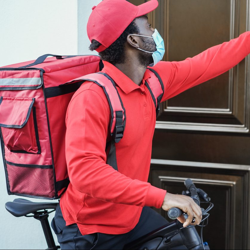 African delivery man with electric bike ringing the doorbell during coronavirus time - Focus on face